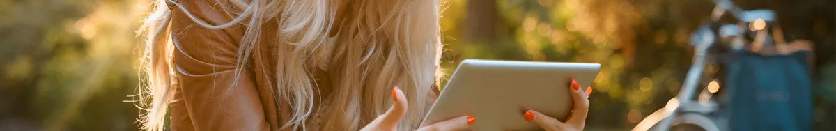 Žena sa pozerá na tablet. V pozadí je bicykel s taškou.