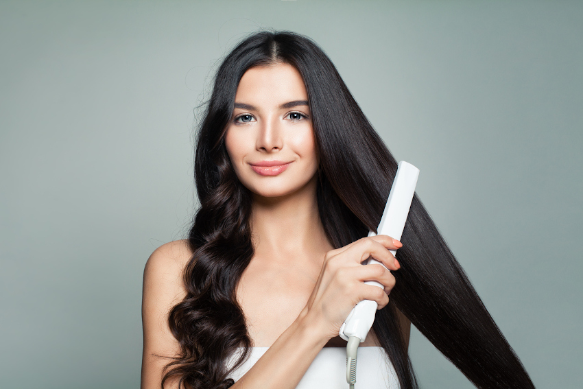 Eine Frau stylt ihre Haare: auf der linken Seite hat sie Locken, auf der rechten glättet sie ihr Haar.