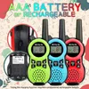 Three colorful walkie-talkies are displayed prominently, with a close-up of batteries and a charging port inset. The background features playful, abstract shapes and patterns. Voir les images du produit