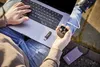 A person is using a laptop outdoors, holding a pair of earbuds and a USB drive. Voir les images du produit