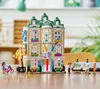 A LEGO Friends art school playset is displayed on a wooden table, with mini-doll figures interacting around it. Podgląd zdjęcia produktu