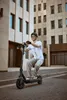 A man rides an electric scooter down a city street with modern buildings in the background. Produktbild-Vorschau