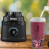 A Ninja blender is shown next to a smoothie in a cup, with liquid being poured into the cup. Produktbild-Vorschau