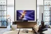 A modern living room with a large TV displaying abstract art, a comfortable armchair, and decorative shelving. Produktbild-Vorschau