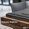 A close-up of a black tablet case on a wooden table, with a blurred background of a chair and room. Produktbild-Vorschau
