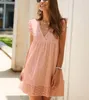 Lächelnde Frau in einem hellen rosa Lochstickerei-Minikleid mit Rüschenärmeln, mehrschichtigen Goldketten und einem weißen Perlenarmband Produktbild-Vorschau