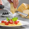 A hand is grating cheese onto a plate of spaghetti with cherry tomatoes and basil. A large block of cheese is visible in the background. Anteprima dell’immagine prodotto
