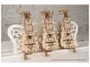 Three wooden UGEARS 3D-puzzles shaped like musical instruments are displayed on a white surface against a brick wall. Produktbild-Vorschau