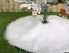 A close-up of a white, fluffy Christmas tree skirt on a grassy surface, with a portion of a flocked Christmas tree visible. Náhľad obrázku produktu