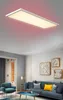 A modern living room with a blue sofa, armchair, and artwork on the wall, illuminated by a rectangular LED panel light with red backlight. Produktbild-Vorschau