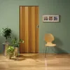 A wooden folding door is shown in a room with plants and a chair. Produktbild-Vorschau