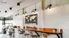 A cafe or bar interior with a long wooden counter, stools, and a world map artwork on the wall. Anteprima dell’immagine prodotto