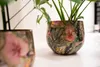 Two decorative plant pots with a tropical leaf and flower pattern sit on a white surface. Voir les images du produit