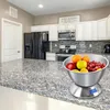 A kitchen counter with a digital scale holding a bowl of fruit, with kitchen cabinets and appliances in the background. Produktbild-Vorschau