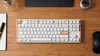 A top-down view of a white mechanical keyboard with wood accents on a wooden desk. Produktbild-Vorschau