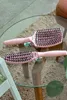 Two pink hairbrushes are placed on a glass table over a woven rug. Produktbild-Vorschau