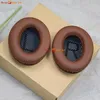 Two brown ear pads for headphones are placed on a light brown cardboard box. Produktbild-Vorschau