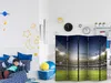 A child is lying on a bed in a room decorated with space-themed wall decals. A room divider with a stadium image is in the foreground. Produktbild-Vorschau