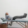 An older woman is lying on a massage table with her legs elevated and encased in a compression device. Produktbild-Vorschau