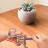 Hands are shown picking a transparent lock on a wooden table, with a potted succulent in the background. Podgląd zdjęcia produktu