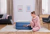 A woman in pajamas is kneeling next to an inflated air mattress, operating its built-in pump. Produktbild-Vorschau