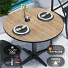 A round table with a wood-like surface set with plates and napkins, a vase of flowers, and glasses. Produktbild-Vorschau