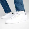 A person wearing white Puma sneakers and blue jeans. Produktbild-Vorschau