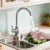 A hand is filling a glass with water from a kitchen faucet over a sink filled with greens. Produktbild-Vorschau
