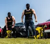 Two men in black balaclavas and black tank tops stand with pressure washers and cars in the background. Produktbild-Vorschau