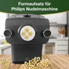 A black pasta maker attachment is shown on a wooden table, with star-shaped pasta pieces in front of it and inside the attachment. The background is a blurred kitchen scene. Náhľad obrázku produktu