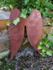 A rusty metal angel wing decoration is placed against a stone wall, with ivy growing around it. Produktbild-Vorschau