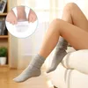 A person's legs are shown wearing gray slouch socks while sitting on a couch. An inset image shows a close-up of a foot being fitted with a gel separator. Podgląd zdjęcia produktu