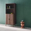 A wooden bookshelf with two doors and four shelves, placed against a green tiled wall. A small copper-colored stool with a decorative object on top is next to the bookshelf. Produktbild-Vorschau