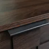 A close-up view of a dark brown wooden furniture piece, likely a TV stand, showing a black handle or drawer pull. Produktbild-Vorschau