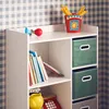 A white shelf unit with books and storage boxes, against a checkered wallpaper. Produktbild-Vorschau