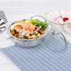A stainless steel pot filled with seafood and vegetables, with a glass lid resting beside it, placed on a blue checkered cloth. Produktbild-Vorschau