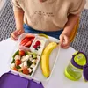 A child's hands are reaching for a b.box lunchbox filled with food, next to a water bottle. Náhľad obrázku produktu