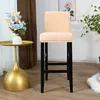 A beige bar stool with a black frame is shown in a room with a golden side table and a bouquet of flowers. Produktbild-Vorschau