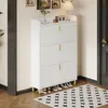 A white shoe cabinet with gold legs is shown in a room with a rug and a door in the background. Produktbild-Vorschau