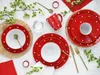 A table setting with red and white polka dot dinnerware, cutlery, and a mug, decorated with white flowers. Produktbild-Vorschau