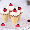 A close-up of several ice cream cones filled with white frosting and decorated with colorful sprinkles and ladybug-shaped candies. Anteprima dell’immagine prodotto