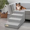A small dog is resting on a couch next to a set of pet stairs. A woven basket with magazines is also visible. Náhled obrázku produktu