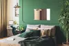 A bedroom scene with a bed, nightstand, and a large plant. Náhľad obrázku produktu