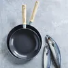 Two frying pans are stacked on a light gray surface, with two fish and scattered salt crystals to the right. Náhled obrázku produktu