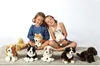 Two young girls are sitting on a rug with several plush toy dogs in front of them and in their arms. Produktbild-Vorschau