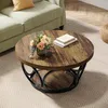 A round coffee table with a wood-grain top and black metal base sits on a patterned rug next to a light green sofa. Anteprima dell’immagine prodotto