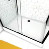 A close-up view of a shower cabin with a white base and white tiled walls, featuring a black drain and glass doors. A yellow bath mat is partially visible in the foreground. Produktbild-Vorschau