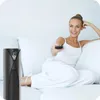 A woman relaxing on a couch with a remote control and a standing fan nearby. Náhled obrázku produktu