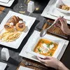 A table setting with a set of white porcelain dishes, including plates, bowls, and serving platters, laid out for a meal. A person's hands are visible, holding a spoon over a bowl of soup. Produktbild-Vorschau
