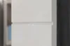 A close-up view of a white cabinet with a gray wood-grain edge. Produktbild-Vorschau